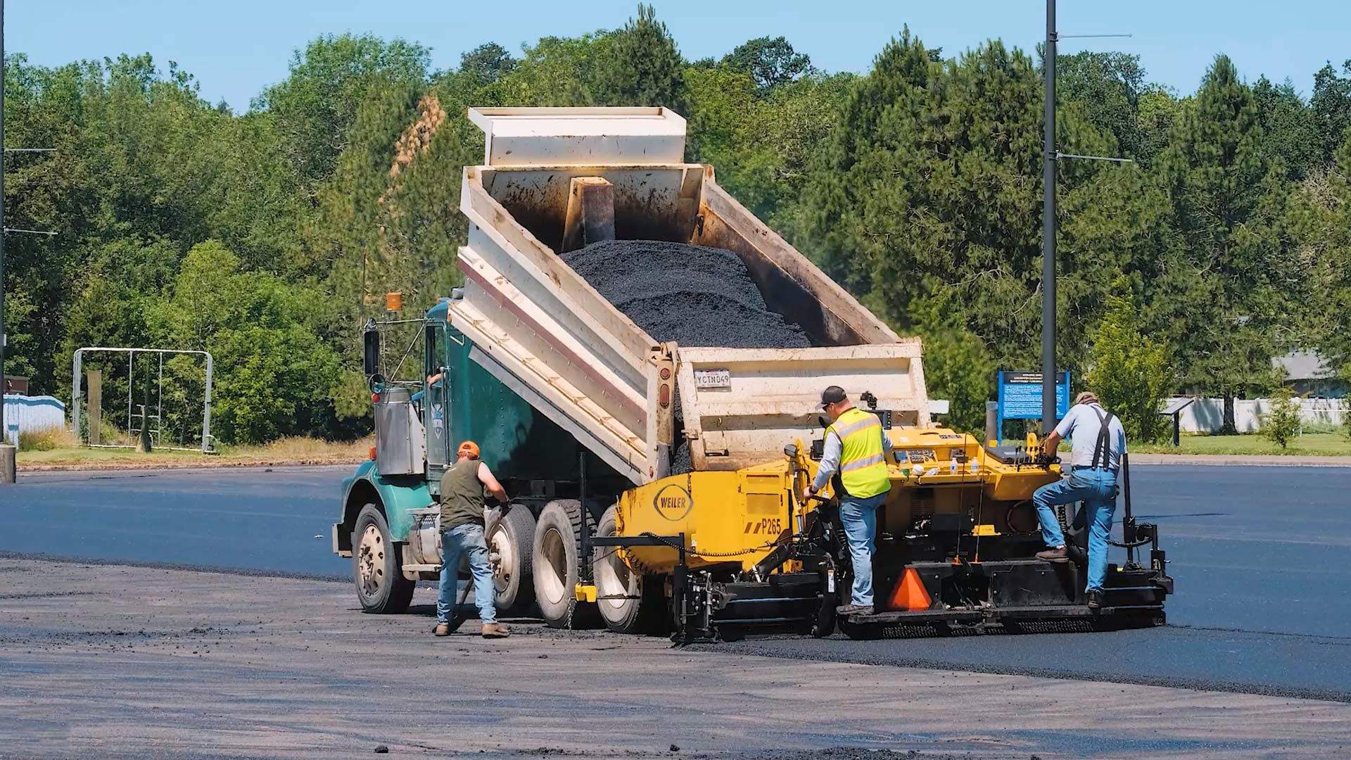 green asphalt dump truck loading asphalt paving machine